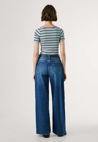 Striped, fitted t-shirt with short sleeves in light blue and dark stripes, paired with wide-leg blue jeans and a studded black belt.