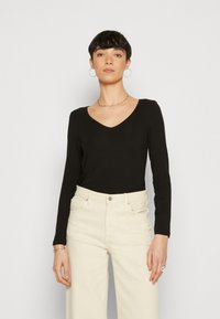 Black long-sleeve V-neck top paired with high-waisted, wide-leg cream trousers. Smooth fabric with a fitted silhouette and minimal detailing.
