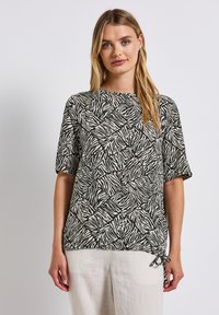 Top a maniche corte in tessuto stampato a righe zebrate in bianco e nero; presenta un colletto rotondo e un dettaglio con fiocco all'orlo.