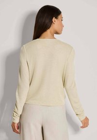 Helle beige Langarm-Strickjacke mit weicher Textur und rundem Ausschnitt, kürzere Passform, kombiniert mit hellfarbigen, fließenden Hosen.