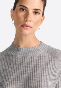 Gray ribbed high-neck sweater featuring a close fit and textured fabric. Gold hoop earrings accent the look.