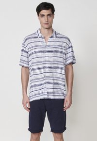 Košeľa s krátkym rukávom a golierom, s vodorovnými modrými a bielymi pruhmi, vyrobená z ľahkej látky. Námornícke šortky s previnutými manžetami.