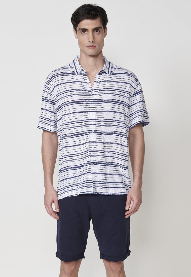 Košeľa s krátkym rukávom a golierom, s vodorovnými modrými a bielymi pruhmi, vyrobená z ľahkej látky. Námornícke šortky s previnutými manžetami.