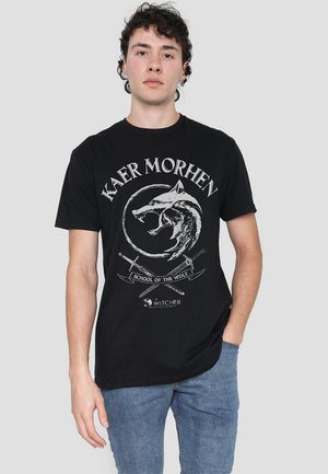 Black cotton t-shirt featuring a front graphic of a wolf’s head within a circle, text reading "KAER MORHEN" and "SCHOOL OF THE WOLF."