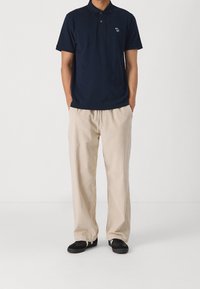 Granatowa koszulka polo z krótkimi rękawami i małym logo, zestawiona z beżowymi szerokimi spodniami z prążkowanej tkaniny oraz czarnymi sneakersami. Prosty, casualowy strój.