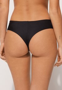 Black bikini bottom featuring a low-rise cut, smooth fabric, minimalistic design, and seamless edges for a clean silhouette.