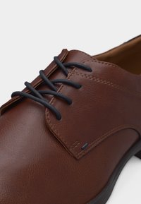 Κοντινό πλάνο καφέ δερμάτινου παπουτσιού φόρεμα με μαύρα κορδόνια, ορατή ραφή και ομαλή υφή σε λευκό φόντο.