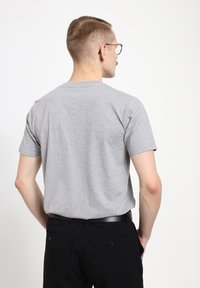 Šedé bavlněné tričko s krátkými rukávy, kulatým výstřihem a uvolněným střihem, nošené s černými kalhotami. Hladká textura, minimalistický design.
