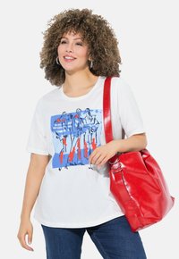 T-shirt blanc avec un imprimé graphique bleu représentant quatre figures, accompagné d'un grand sac à main en cuir rouge avec des accents en métal argenté.