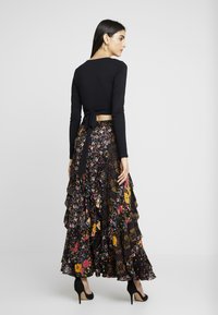 Top preto de manga longa combinado com uma saia maxi floral em camadas, com volantes, uma mistura de padrões coloridos e um detalhe amarrado nas costas.