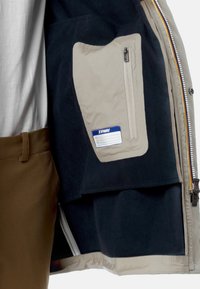 Giacca in pile navy con tasca beige con zip, caratterizzata da un'etichetta blu. L'interno presenta texture a contrasto e una chiusura con zip.