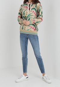 Beige hoodie med blommönster och dragsko, i kombination med ljusblå skinny jeans och vita sneakers. Har ribbade manschetter och nederkant.