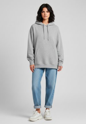 Grijze hoodie met een voorzak, gecombineerd met opgerolde lichtblauwe jeans en witte sneakers. Gladde stof, relaxte pasvorm.