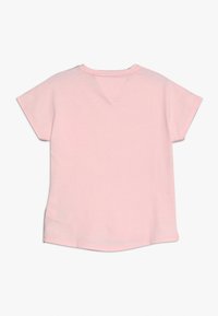 Camiseta de algodón rosa con mangas cortas, dobladillo redondeado y detalle de costura en la parte posterior. Textura suave, diseño casual, sin patrones ni acentos adicionales.