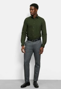 Donkergroen overhemd met lange mouwen, gecombineerd met grijze gestructureerde broek en zwarte formele schoenen. Eenvoudig ontwerp zonder zichtbare patronen.
