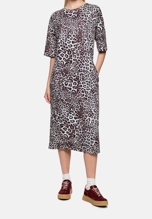 Frau trägt ein midilanges Kleid mit Leopardenmuster und ellbogenlangen Ärmeln, weiße Socken und bordeauxrote Sneakers mit Gummisohlen.