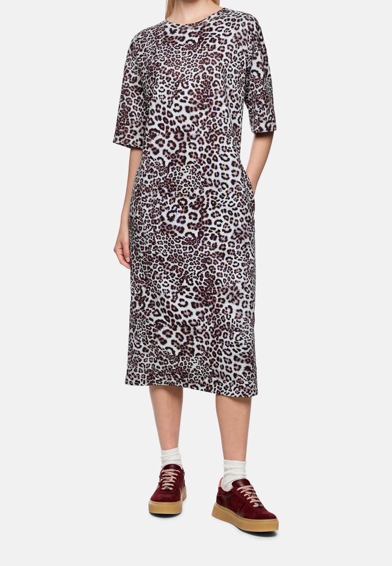 Femme portant une robe mi-longue à imprimé léopard avec des manches au niveau des coudes, des chaussettes blanches et des baskets bordeaux avec semelles en gomme.