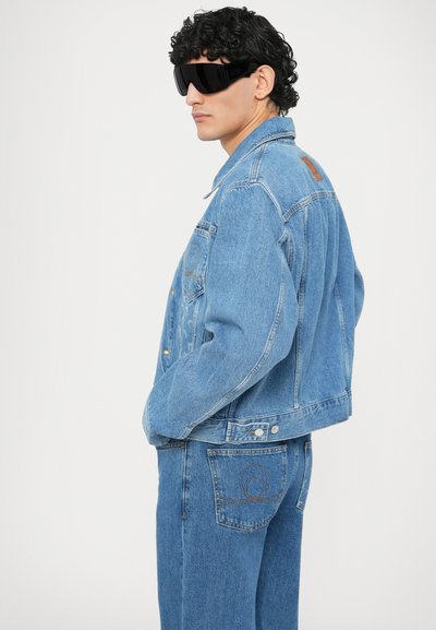 Svetlo modra denim jakna s skrajšanim krojem, z žepi spredaj, teksturirano obdelavo in usnjenim poudarkom na zadnji strani.