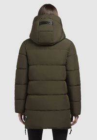Parka c�ăptușită de culoare verde măsliniu cu glugă, având secțiuni orizontale cusute și un patch cu marcă pe spate. Snururi ajustabile la tiv.