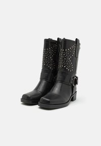 Botas de tobillo de cuero negro con tachuelas plateadas decorativas, una correa con detalle de hebilla y un tacón bajo en bloque. Textura suave.