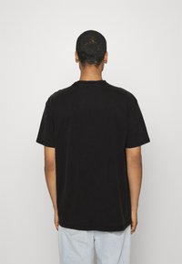 Camiseta de algodón negra con mangas cortas, cuello redondo y costuras visibles. La camiseta se lleva al revés, mostrando la parte trasera lisa sin gráficos ni patrones.
