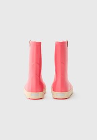 Un par de botas de lluvia de goma rosas con suelas beige, vistas desde la parte de atrás sobre un fondo blanco liso.