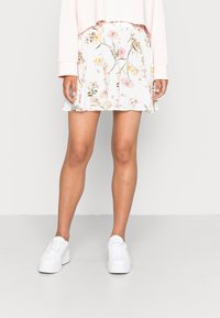Jupe à motif floral blanche avec une taille élastique, associée à des baskets blanches. La jupe est en tissu doux et possède une coupe évasée.