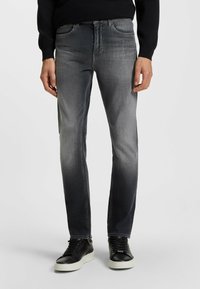 Jeans in denim grigio con vestibilità dritta, caratterizzati da un lavaggio sbiadito, design a cinque tasche e rivetti in metallo, abbinati a sneakers nere.