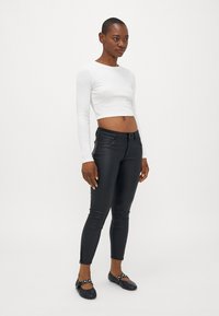 Fehér, hosszú ujjú crop top, fekete, slim-fit nadrág bokazippel, és lapos fekete cipők fehér pöttyökkel. Sima szövet textúrák.
