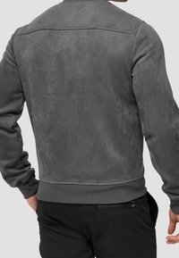 Veste en daim gris à texture lisse, avec des poignets et un ourlet côtelés, présentant un design simple sans quincaillerie ni ornements visibles.