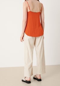 Top sin mangas naranja con tirantes ajustables, combinado con pantalones de pierna ancha crema con rayas verticales color óxido y sandalias planas.