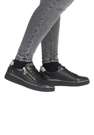 Zwarte sneakers met een gestructureerde bovenkant met een geometrisch patroon, gouden accenten, ritsdetails en een rubberen zool, gecombineerd met grijze skinny jeans.