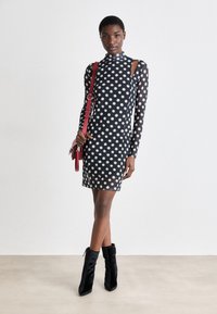 Ilgi piedurkņu polka-puntu kleita melnā krāsā ar rozā un baltām punktiem, ar atklātām plecu detaļām, saskaņota ar melniem potīšu zābakiem un sarkanu rokassomu.
