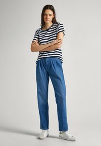 Camiseta a rayas en azul marino y blanco combinada con pantalones de mezclilla azules y zapatillas blancas; ajuste casual con mangas cortas y estilo relajado.