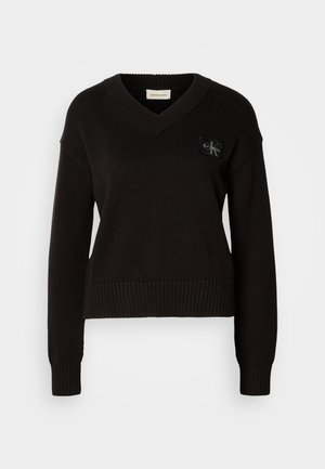 Schwarzer Strickpullover mit V-Ausschnitt, gerippten Bündchen und Saum. Auf der oberen linken Vorderseite befindet sich ein rechteckiges Logopatch. Weiche Textur.