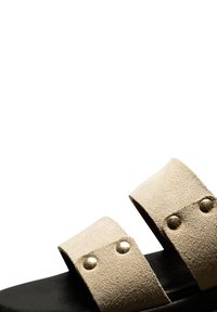 Two-strap sandals featuring a beige suede upper with gold studs, black rubber sole, and flat design. Suitable for casual wear.