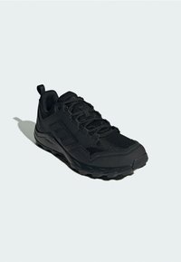 Zwarte sportieve schoen met een bovenwerk van mesh, een gestructureerde rubberen zool en een versterkte neus. Heeft een vetersluiting en een trekband bij de hiel.