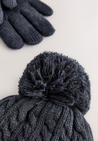 Gebreide marineblauwe muts met een gestructureerd kabelpatroon en een pluizige pompon, gecombineerd met bijpassende nauwsluitende handschoenen met geribbelde boorden.