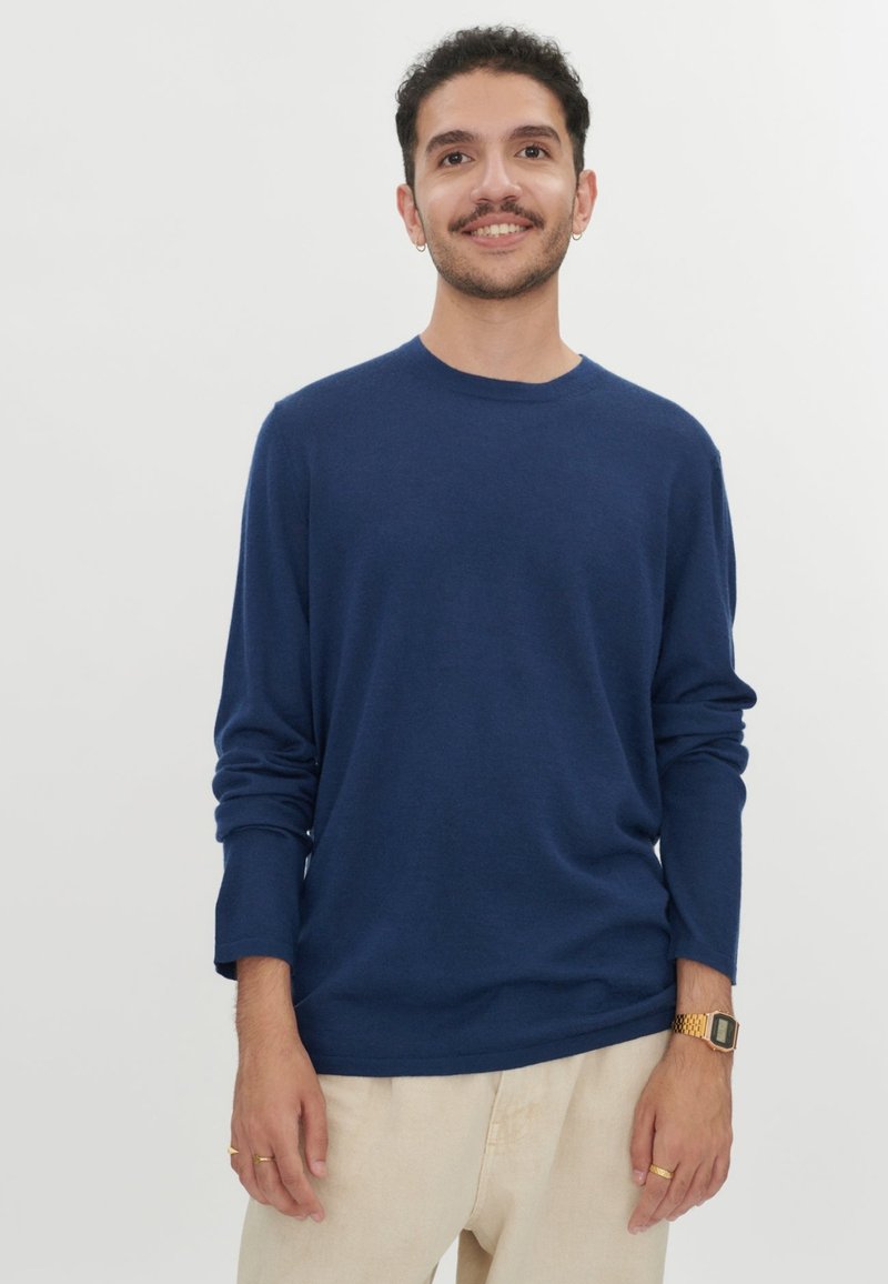 Marineblaues Langarm-T-Shirt aus weichem Stoff, mit Rundhalsausschnitt und lockerem Schnitt. Kombiniert mit hellen Hosen, minimalistisch im Design.