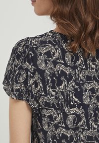 Blusa blu navy con maniche corte a sbuffo, caratterizzata da un motivo animale bianco. Il tessuto testurizzato aggiunge interesse visivo.