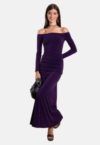 Robe violette dénudée sur les épaules, avec des manches longues et des détails froncés, faite d'un tissu lisse et extensible, associée à une pochette noire texturée.
