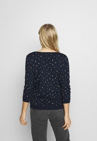 Marinblå tröja med spridda flerfärgade mönster, långa ärmar och båtkrage. Mjuk textur, figurnära silhuett och ribbade ärmslut.