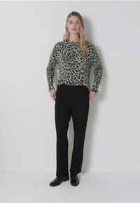 Leopardmönstrad tröja med långa ärmar, ihop med svarta byxor och blanka svarta skor, presenterad mot en neutral bakgrund.