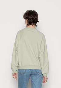 Felpa verde menta con collo a giro, maniche raglan e polsini a costine. Tessuto morbido con vestibilità rilassata, indossata con jeans blu.
