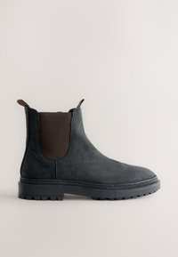 Schwarzer Chelsea-Lederstiefel mit braunen elastischen Seitenteilen, Zuglaschen und dicker Gummisohle auf hellem, schlichten Hintergrund.