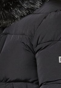 Svart isolerad puffjacka med glansig yta, rynkad textur och krage i fuskpäls. Inkluderar silverfärgade detaljer.