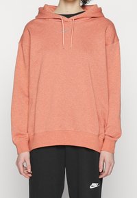 Korallrosa hoodie med känguruficka, dragsko och logotypdetalj. Tillverkad av mjukt tyg med avslappnad passform och ribbade ärmar.