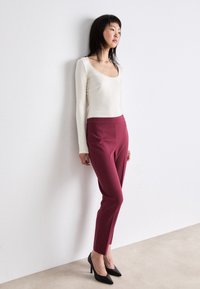 Witte lange mouw top met een ronde hals, gecombineerd met slim-fit bordeauxrode broek en zwarte puntige hakken. Gladde stoftexturen.