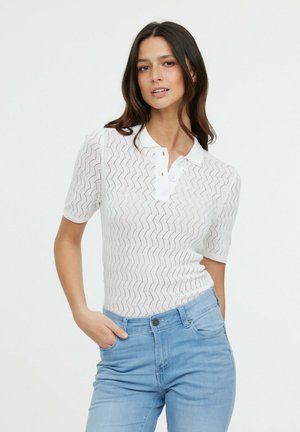 Polo shirt blanc à manches courtes avec un motif ondulé texturé, doté d'un col et d'une fermeture à trois boutons. Associé à un jean bleu clair.