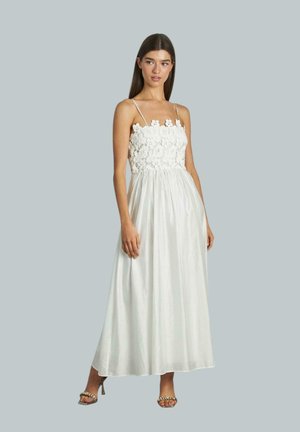 Weißes Maxikleid mit ärmellosem Spitzenoberteil, Spaghettiträgern und fließendem Rock; glatte Textur. Model trägt Sandalen mit Riemchen, heller Hintergrund.